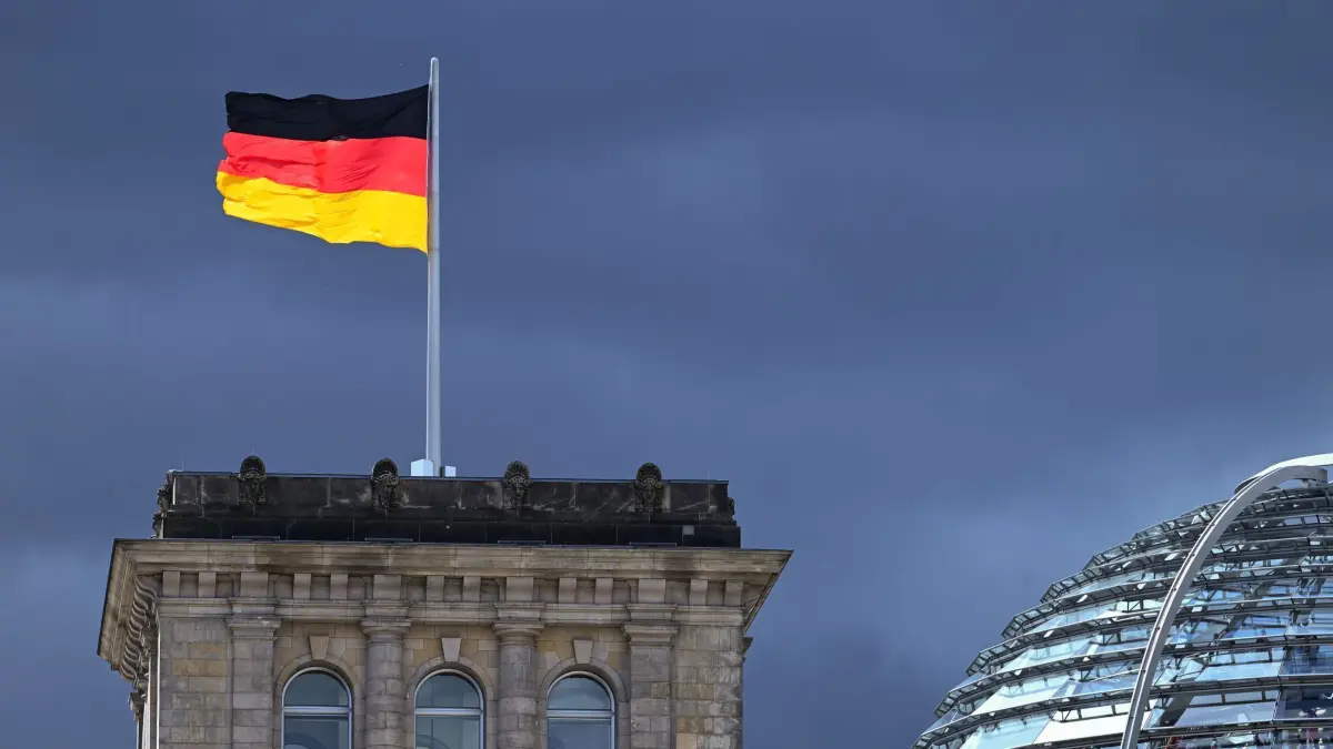 Reichstagsgebäude: ARCHIV - 03.08.2023, Berlin: Eine der Flaggen auf dem Reichstag leuchtet bei starkem Wind wehend vor der Kulisse von dunklen Regenwolken. (zu dpa: «Steinmeier macht Weg für Neuwahl frei») Foto: Soeren Stache/dpa +++ dpa-Bildfunk +++
