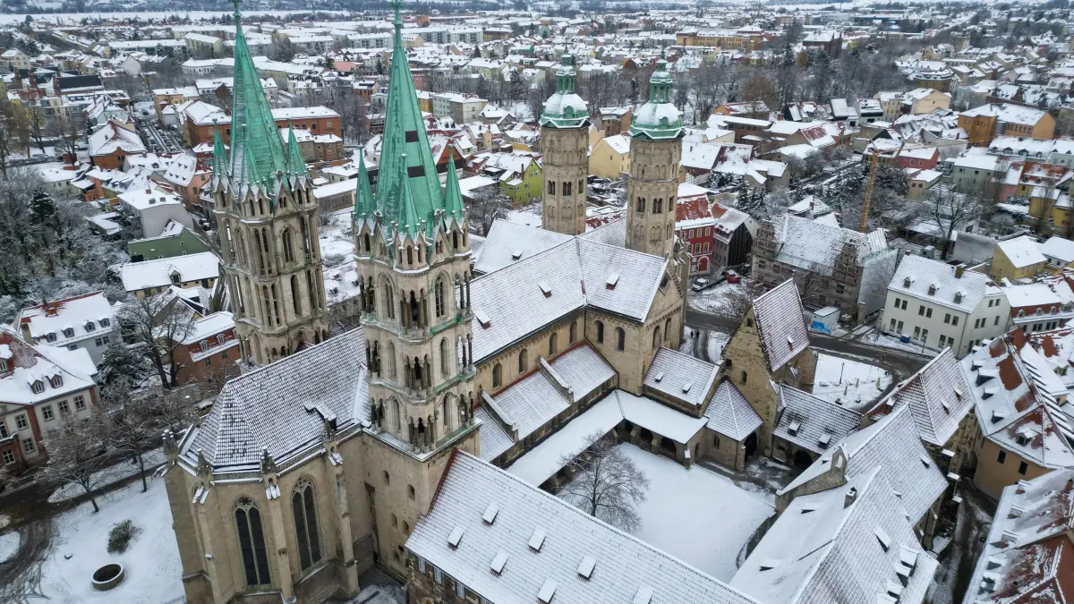 Cranach-Triegel-Altar kehrt in den Naumburger Dom zurück: ARCHIV - 29.11.2023, Sachsen-Anhalt, Naumburg (Saale): Schnee bedeckt den historischen Dom in Naumburg. Nach hitzigen Diskussionen kehrt nach rund einem Jahr jetzt der Cranach-Triegel-Altar in den Westchor des Gotteshauses zurück. Der Leipziger Maler Michael Triegel hatte das 1519 von Lukas Cranach d. Ä. geschaffene Kirchengemälde wieder vervollständigt und den Mittelteil neu geschaffen. Nach der Altarweihe im Sommer 2022 war plötzlich der Standort im Westchor zwischen den berühmten Stifterfiguren umstritten. Zunächst bis 2025 ist er nun wieder an prominenter Stelle im Naumburger Dom zu sehen. (Luftaufnahme mit Drohne). (zu dpa: «Einbruch im Naumburger Dom») Foto: Hendrik Schmidt/dpa +++ dpa-Bildfunk +++
