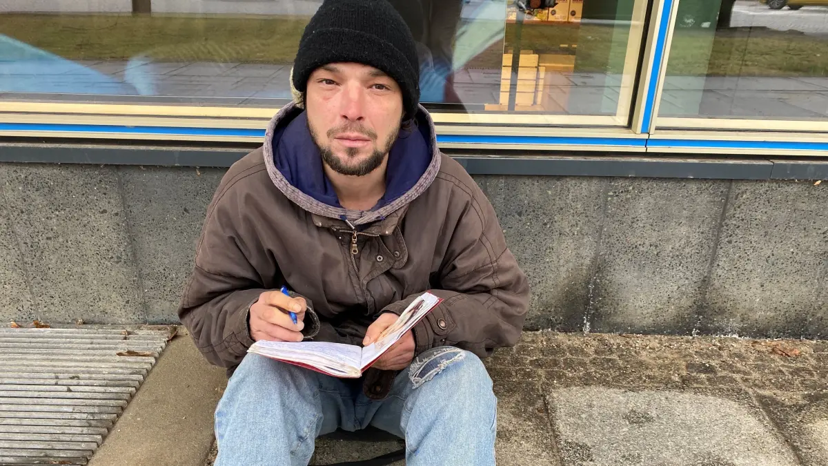 Notiert Gedanken und Erinnerungen: Marcel Guido Petschick in der Lindenallee in Eisenhüttenstadt. Neben ihm steht ein Plastebecher für Spenden. Der 42-jährige Obdachlose sitzt bei Wind und Wetter dort.