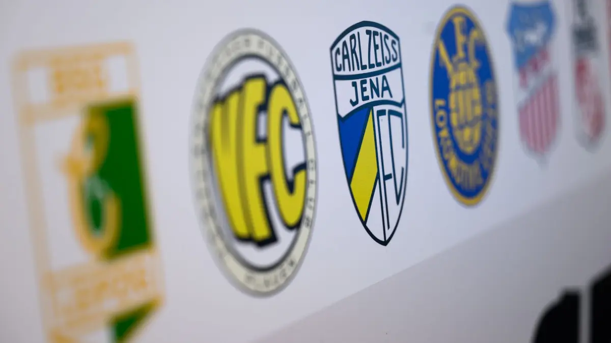 Nordost-Regionalligisten wollen Direktaufstieg: 12.02.2025, Sachsen, Chemnitz: Die Logos von insgesamt 17 Vereinen aus der Fußball-Regionalliga Nordost, darunter BSG Chemie Leipzig (l-r), VFC Plauen, FC Carl Zeiss Jena, 1. FC Lok Leipzig und FSV Zwickau sind am Podium einer Pressekonferenz zu sehen. Die Vereine wollen mit der Aufstiegsreform 2025 einmal mehr ihre Interessen durchsetzen, damit der Meister des Nordostdeutschen Fußballverbands (NOFV) endlich direkt in die 3. Liga aufsteigt. Ziel ist zudem eine grundlegende Veränderung, die eine faire und integere Wettbewerbsstruktur im gesamtdeutschen Fußball schafft. Foto: Hendrik Schmidt/dpa +++ dpa-Bildfunk +++