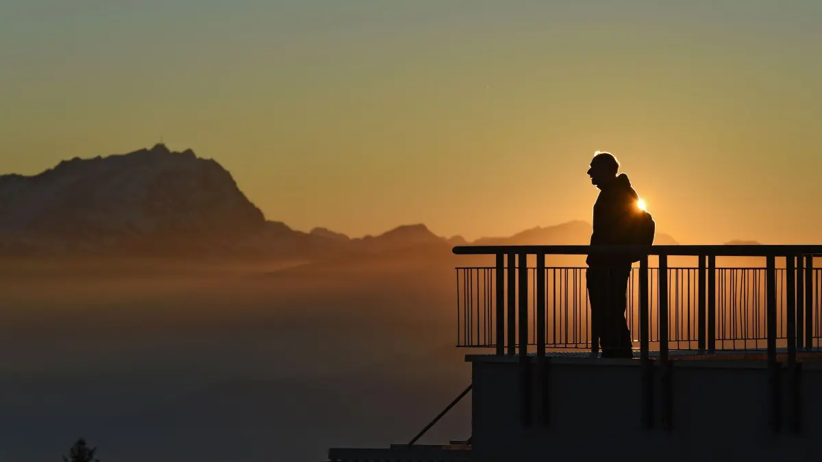 dpatopbilder Ein Wanderer schaut sich am 02.12.2015 auf dem Pfänder (Vorarlberg in Österreich) den Sonnenuntergang hinter den Alpen an, während im Hintergrund der Schnee bedeckte Berg Säntis (l) in der Schweiz zu sehen ist. Foto: Felix Kästle/dpa ++ +++ dpa-Bildfunk +++