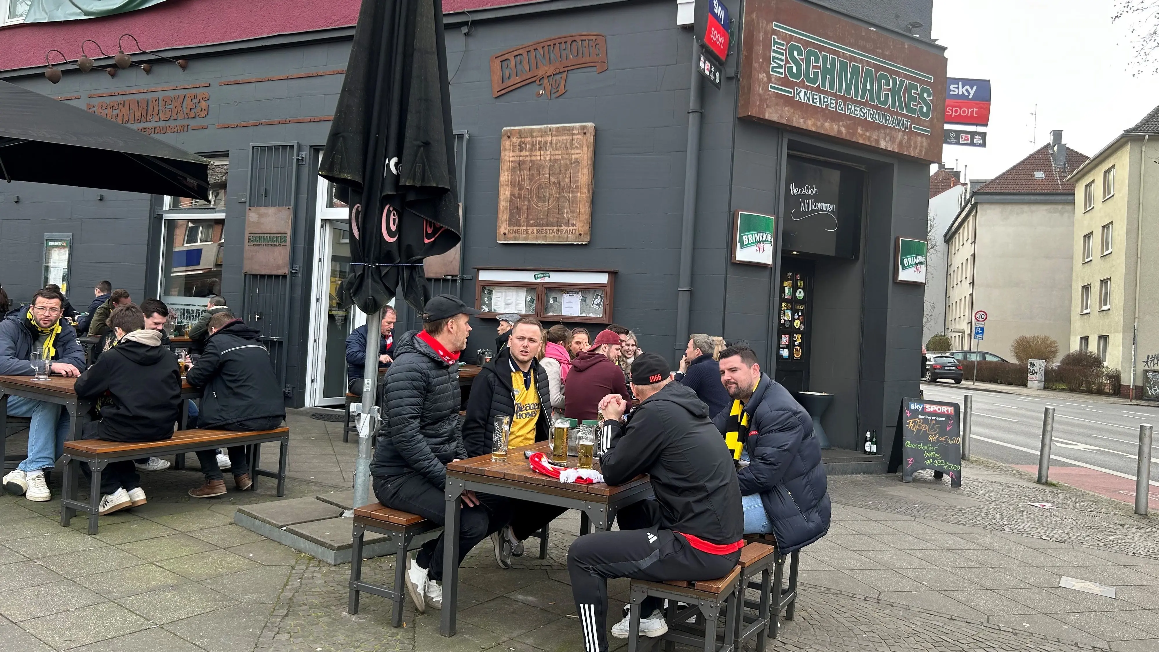 Vor dem Restaurant Mit Schmackes von Weltmeister Kevin Großkreutz sitzen Fans von Union Berlin und Borussia Dortmund gemeinsam am Tisch.