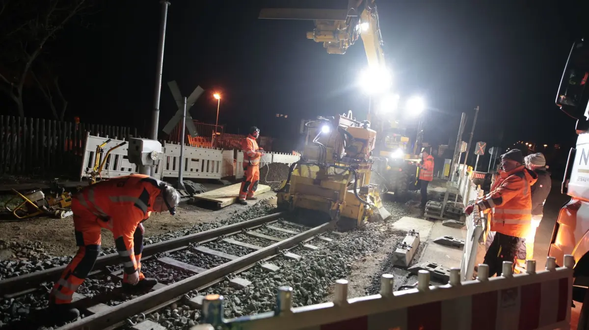 Bauarbeiten mit Spezialmaschine bei den Harzer Schmalspurbahnen: 13.03.2025, Sachsen-Anhalt, Wernigerode: Mitarbeiter eines Gleisbaubetriebes arbeiten an einem Bahnübergang der Harzer Schmalspurbahnen GmbH in Wernigerode. Auf der Nachtbaustelle wird unter anderem der Schotterbelag unter den Bahnschwellen mit einer Spezialmaschine verdichtet. Die HSB unterhält auf ihrem Gleisnetz über 100 Bahnübergänge die nach und nach umgebaut und mit neuen Signalanlagen sowie Schranken ausgerüstet werden. Die Arbeiten an den Bahnübergangsstellen werden in den kommenden Tagen weiter fortgesetzt. Foto: Matthias Bein/dpa +++ dpa-Bildfunk +++