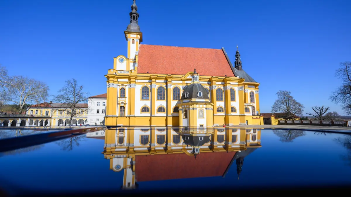 Frühling im barocken Klostergarten: 20.03.2025, Brandenburg, Neuzelle: Die katholische Kirche vom Kloster Neuzelle spiegelt sich in einem Autodach. Das Kloster Neuzelle, rund zehn Kilometer südlich von Eisenhüttenstadt, ist das einzige vollständig und einschließlich der Außenanlagen erhaltene Zisterzienserkloster Brandenburgs und eine der wenigen unzerstörten Klosteranlagen in Deutschland und Europa. Foto: Patrick Pleul/dpa/ZB - Honorarfrei nur für Bezieher des Dienstes ZB-Funkregio Ost +++ ZB-FUNKREGIO OST +++