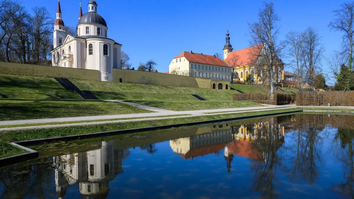 Frühling im barocken Klostergarten: 20.03.2025, Brandenburg, Neuzelle: Blick aus dem Klostergarten auf die evangelische Kirche (l) und dahinter die katholische Kirche. Das Kloster Neuzelle, rund zehn Kilometer südlich von Eisenhüttenstadt, ist das einzige vollständig und einschließlich der Außenanlagen erhaltene Zisterzienserkloster Brandenburgs und eine der wenigen unzerstörten Klosteranlagen in Deutschland und Europa. Foto: Patrick Pleul/dpa/ZB - Honorarfrei nur für Bezieher des Dienstes ZB-Funkregio Ost +++ ZB-FUNKREGIO OST +++