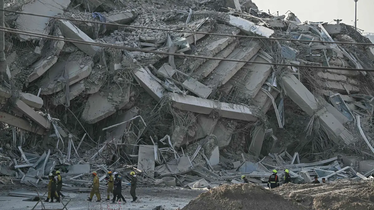 Rescue workers walk past debris of a construction site after a building collapsed in Bangkok on March 28, 2025, following an earthquake. A powerful earthquake rocked central Myanmar on March 28, buckling roads in capital Naypyidaw, damaging buildings and forcing people to flee into the streets in neighbouring Thailand. (Photo by Lillian SUWANRUMPHA / AFP)