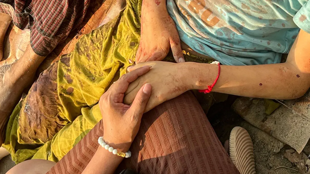 A earthquake survivor holds the hand of a relative as lying on the ground of the compound of a hospital in Naypyidaw on March 28, 2025, after an earthquake in central Myanmar. A powerful earthquake rocked central Myanmar on March 28, buckling roads in capital Naypyidaw, damaging buildings and forcing people to flee into the streets in neighbouring Thailand. (Photo by Sai Aung MAIN / AFP)