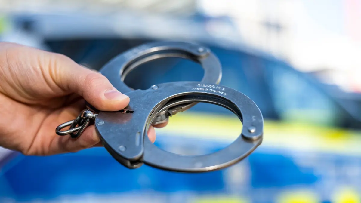 Handschellen vor Polizeiwagen - Symbolbild