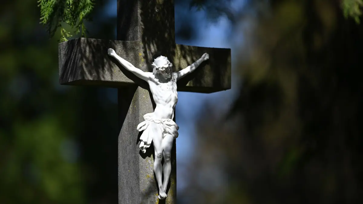 ARCHIV - 11.04.2022, Österreich, Salzburg: An einem Grab steht eine Darstellung des gekreuzigten Jesus. Der Karfreitag zählt zu den wichtigsten Tagen des Christentums, an diesem Tag wird der Kreuzigung und des Todes Jesus Christus gedacht. (zu dpa: «Passionsspiele in Osthessen - «Unserem Herrgott Danke sagen»») Foto: Barbara Gindl/APA/dpa +++ dpa-Bildfunk +++