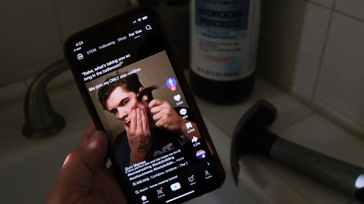 'Toxic beauty': Rise of 'looksmaxxing' influencers : This illustration photo shows a video of male TikTok influencer hammering his cheekbone, playing on a smartphone in a bathroom next to a bottle of hydrogen peroxide and a hammer in Los Angeles, April 11, 2025. Hankering for a perfectly angular jaw, a male TikTok influencer hits his cheekbones with a hammer -- part of the popular online ?looksmaxxing? trend that promotes unproven and often dangerous techniques to boost sexual appeal. Looksmaxxing influencers -- part of an online ecosystem dubbed the "manosphere" -- have surged in popularity across social media, capitalizing on the insecurities of young men eager to boost their physical attractiveness to women. (Photo by Chris DELMAS / AFP)