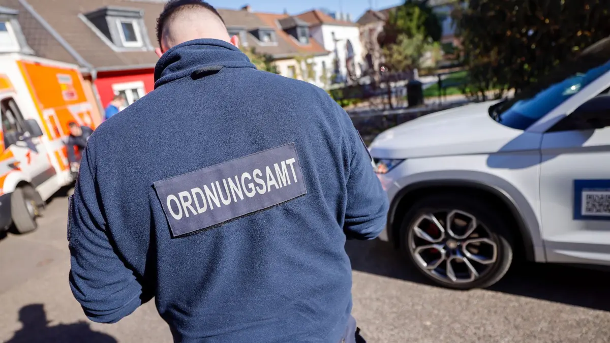 Feuerwehr kontrolliert Rettungswege - Ordnungsamt: PRODUKTION - 07.04.2025, Nordrhein-Westfalen, Köln: Ein Mitarbeiter des Ordnungsamts kontrolliert Autos, die in einer engen Straße verkehrsbehindert geparkt haben. Die Feuerwehr fährt Straßen ab, um zu überprüfen, ob Rettungswege frei sind oder durch Falschparker behindert werden. (zu dpa: «Jede Sekunde zählt - Falschparker behindern die Feuerwehr») Foto: Thomas Banneyer/dpa +++ dpa-Bildfunk +++