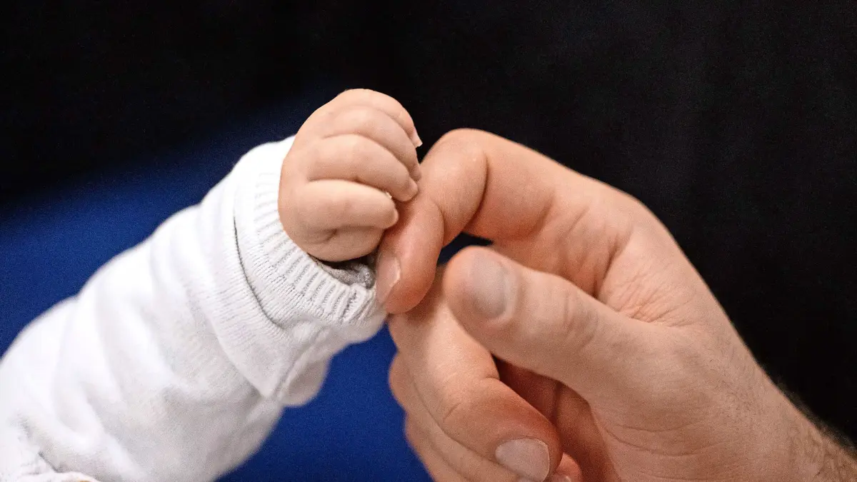 SYMBOLBILD - 24.11.2023, Baden-Württemberg, Stuttgart: Ein Vater berührt während eines Infant Handling Kurses die Hand seines Kindes. Die Geburtenrate im Südwesten ist im vergangenen Jahr unter die Marke von 100.000 Neugeborenen gesunken. (zu dpa: «Zahl der Geburten im Südwesten auf Tiefstand») Foto: Marijan Murat/dpa +++ dpa-Bildfunk +++