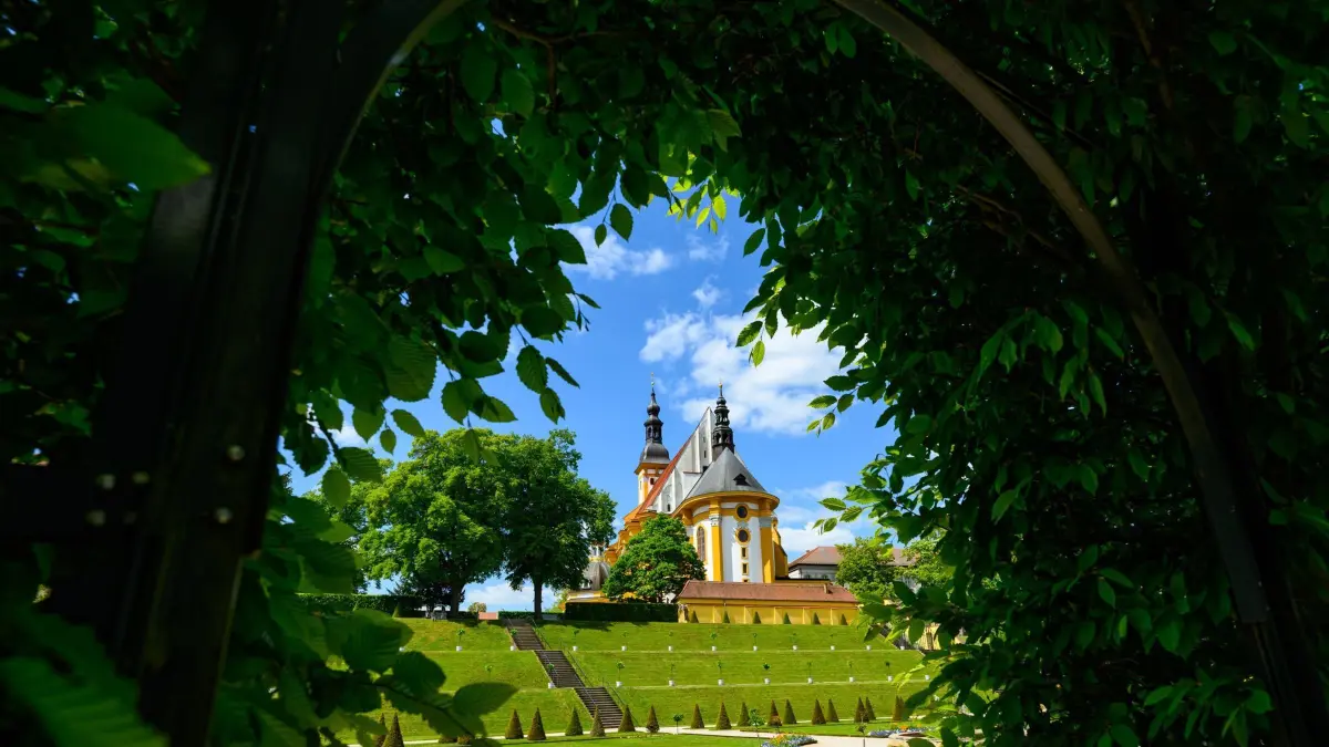 Sonniges Wetter über barocken Klostergarten: 12.05.2025, Brandenburg, Neuzelle: Blick aus dem Klostergarten zur katholische Kirche. Das Kloster Neuzelle, rund zehn Kilometer südlich von Eisenhüttenstadt, ist das einzige vollständig und einschließlich der Außenanlagen erhaltene Zisterzienserkloster Brandenburgs und eine der wenigen unzerstörten Klosteranlagen in Deutschland und Europa. Foto: Patrick Pleul/dpa - Honorarfrei nur für Bezieher des Dienstes ZB-Funkregio Ost +++ ZB-FUNKREGIO OST +++