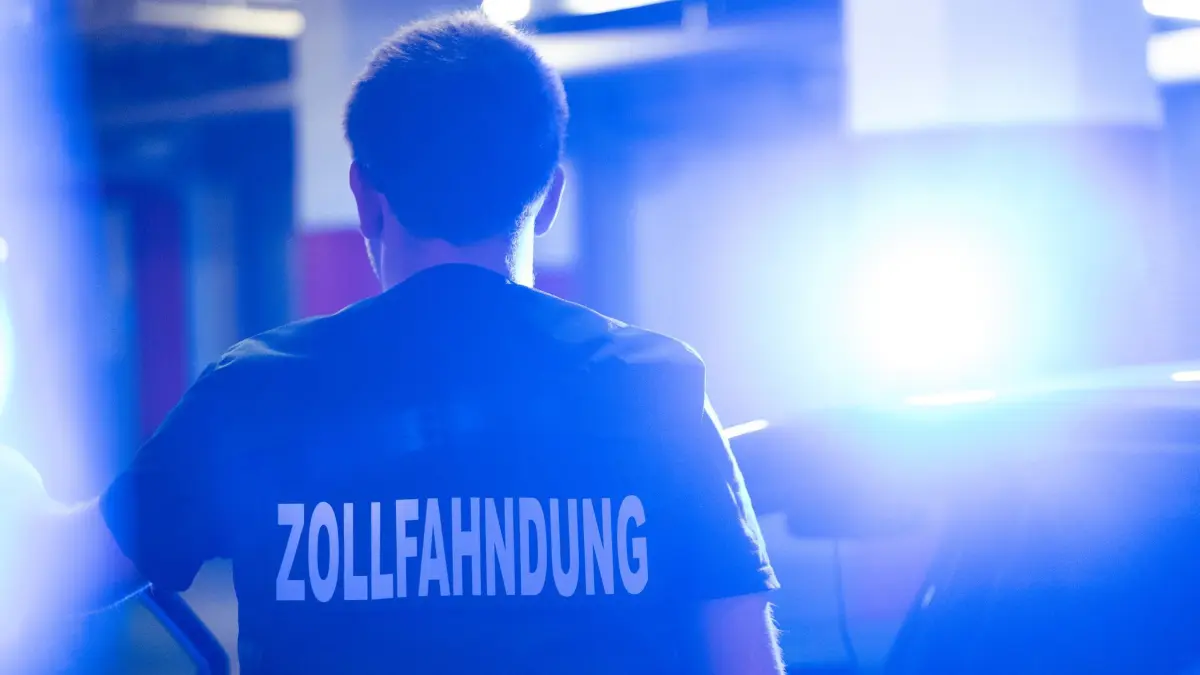 Zollfahndung: ILLUSTRATION - 12.05.2025, Bayern, München: Ein Zollfahnder steht neben einem Auto mit Blaulicht auf dem Dach. (zu dpa: «Großrazzia wegen Schmuggel von Shishatabak») Foto: Leonie Asendorpf/dpa +++ dpa-Bildfunk +++