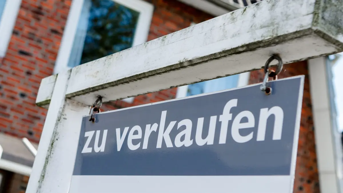 Ein Schild mit der Aufschrift „zu verkaufen“ steht vor einem Haus