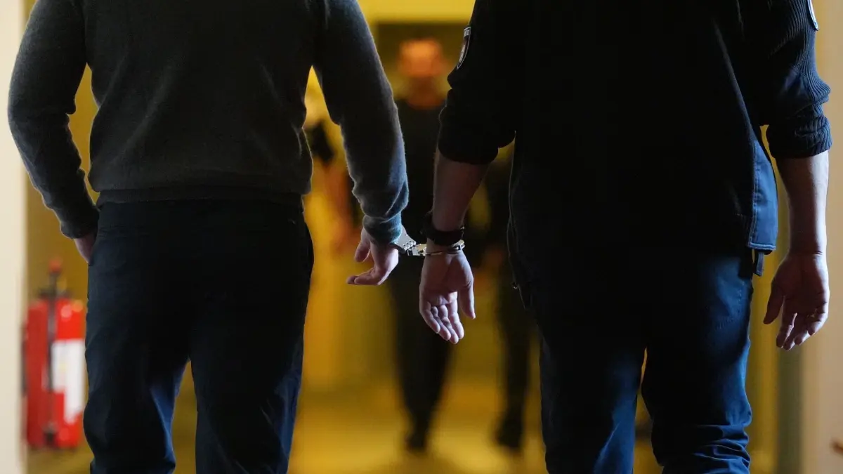 Prozess wegen erpresserischen Menschenraubs: 22.05.2025, Hamburg: Die Angeklagten (l und hinten M) werden in Handschellen von Justizbeamten über einen Flur zum Sitzungssaal im Strafjustizgebäude gebracht. Der Prozess wegen erpresserischen Menschenraubs gegen eine angeklagte Frau und zwei angeklagte Männer hat begonnen. Am 01.07.2024 soll die 37-jährige Angeklagte einen Mann unter einem Vorwand in ihre Wohnung in Hamburg-Bergedorf gelockt haben, um geplante Misshandlungen und eine Erpressung durch die Mitangeklagten und einen unbekannten Mittäter zu ermöglichen. Der Mann soll gefesselt, geschlagen, bedroht und – unter anderem mit einer Schusswaffe – zur Herausgabe von 150.000 Euro gezwungen worden sein. Foto: Marcus Brandt/dpa +++ dpa-Bildfunk +++