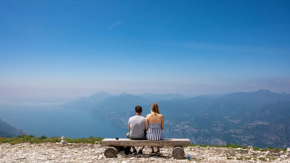 Ein Pärchen sitzt auf einer Bank auf dem Berg Monte Baldo und schaut hinunter auf den Gardasee. +++ dpa-Bildfunk +++