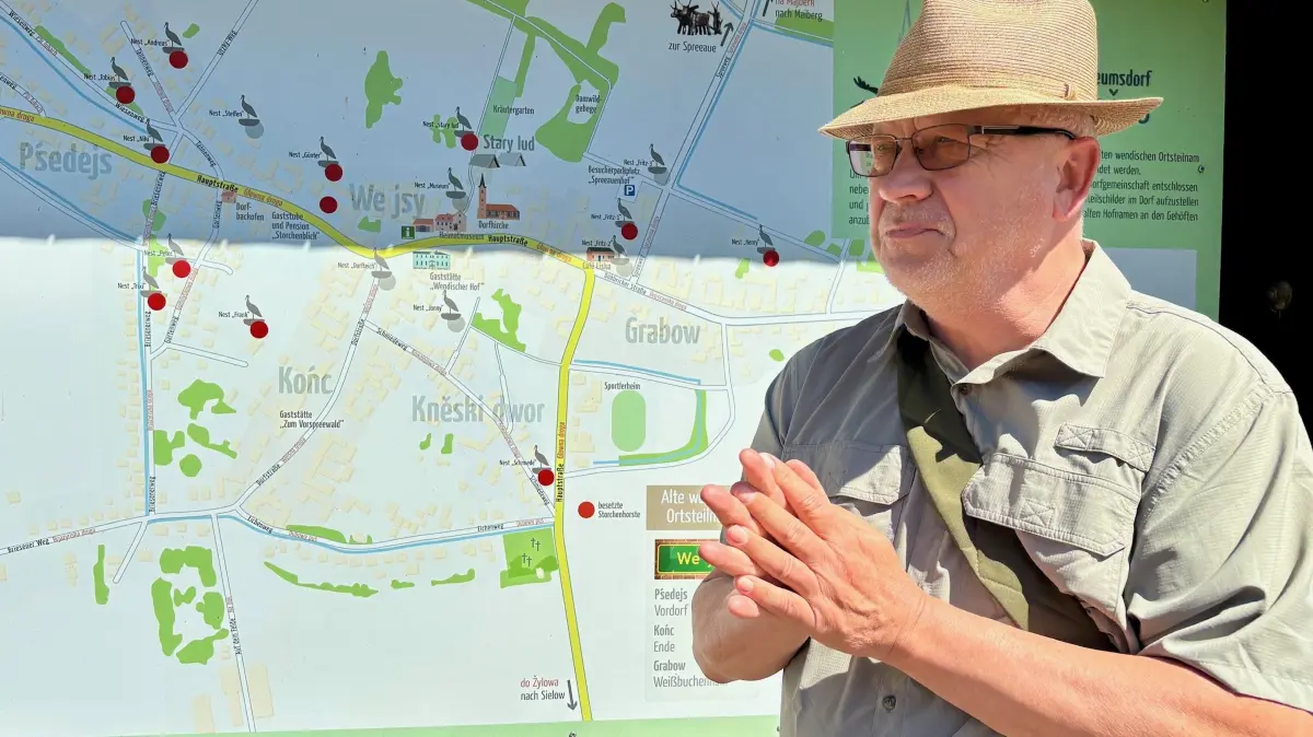 Albrecht Hanke ist Storchenführer in Dissen (Spree-Neiße). Er steht vor der Infotafel, auf der alle Horste im Spreewalddorf eingezeichnet sind. Jeden Donnerstag gibt es geführte Touren.