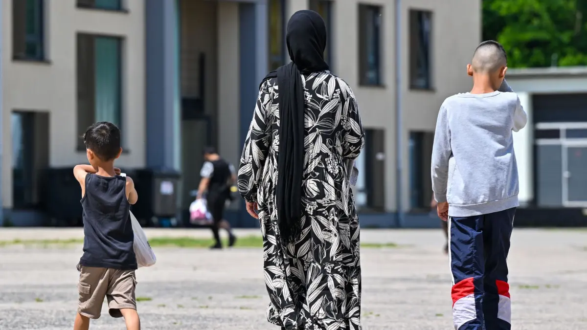 Erstaufnahmeeinrichtung für Asylbewerber: ARCHIV - 18.06.2024, Brandenburg, Eisenhüttenstadt: Eine Migrantin und ihre zwei Kinder gehen über das Gelände der Zentralen Erstaufnahmeeinrichtung für Asylbewerber (ZABH) des Landes Brandenburg. (zu dpa: «Zahl der Schutzsuchenden in Deutschland steigt leicht») Foto: Patrick Pleul/dpa +++ dpa-Bildfunk +++