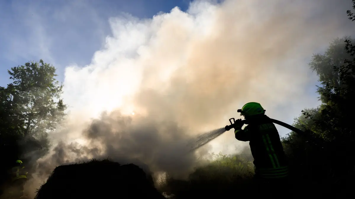 Brennende Heuballen behindern Sicht auf Autobahn A2: 30.06.2025, Niedersachsen, Peine: Feuerwehrkräfte löschen brennende Heuballen. Knapp 40 brennende Heuballen direkt neben der Autobahn A2 haben am Morgen für eine starke Rauchentwicklung und Sichtbehinderungen gesorgt. Foto: Julian Stratenschulte/dpa +++ dpa-Bildfunk +++