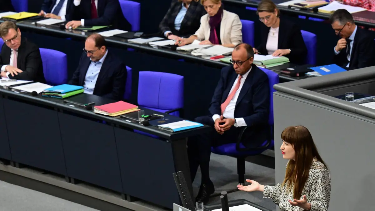 Parliamentary group leader of Germany's The Left (Die Linke) party Heidi Reichinnek addresses parliamentarians while German Chancellor Friedrich Merz listens in the background during a general debate on the budget of the Chancellery at the Bundestag, the lower house of parliament, in Berlin, on July 9, 2025, while the . (Photo by Tobias SCHWARZ / AFP)