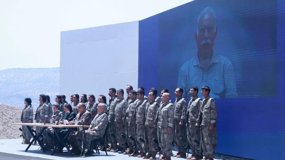 Kurdistan Workers' Party (PKK) commanders and fighters stand in front of a picture of jailed leader and founder of the PKK Abdullah Ocalan during a ceremony in Sulaimaniyah, in Iraq's autonomous Kurdistan region, on July 11, 2025. Thirty PKK fighters destroyed their weapons at a ceremony in Iraqi Kurdistan on July 11, two months after the Kurdish rebels ended their decades-long armed struggle against the Turkish state. The ceremony marks a turning point in the transition of the Kurdistan Workers' Party (PKK) from armed insurgency to democratic politics, as part of a broader effort to draw a line under one of the region's longest-running conflicts. (Photo by Shwan MOHAMMED / AFP)