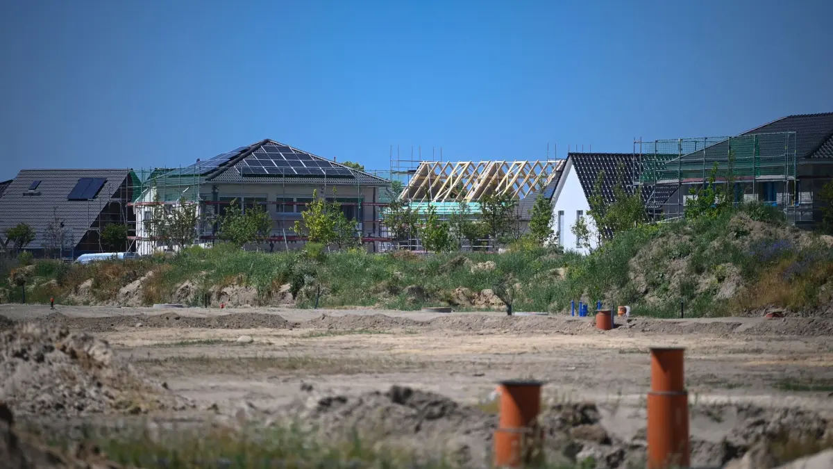 Einfamilienhäuser und Rohbauten stehen hinter einer Baustelle: ARCHIV - 14.06.2021, Brandenburg, Ludwigsfelde: Bodenverhältnisse, Tragfähigkeit, Grundwasserstand: Ein Baugrundgutachten kann private Bauherren vor hohen Kosten und Risiken bewahren. (zu dpa: «Grundstücksverkäufe steigen wieder in Brandenburg») Foto: Soeren Stache/dpa-Zentralbild/dpa-tmn +++ dpa-Bildfunk +++