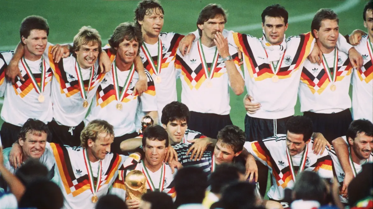 Die deutsche Mannschaft stellt sich nach der Siegerehrung bei der Fußball-Weltmeisterschaft im Olympiastadion von Rom zum Gruppenbild aufg (Hinten, l-r) Stefan Reuter, Jürgen Klinsmann, Frank Mill, Guido Buchwald, Paul Steiner, Thomas Berthold, Andreas Köpke. Vorn (l-r) Sepp Maier, Andreas Brehme, Lothar Matthäus (mit der WM-Trophäe), Karl-Heinz Riedle, Bodo Illgner, Uwe Bein, Günter Hermann. Das deutsche Team bezwang im Finale Argentinien mit 1:0. (zu "Köpke wird 60: «Dankbar» für ein Fußball-Leben mit Höhen und Tiefen") +++ dpa-Bildfunk +++