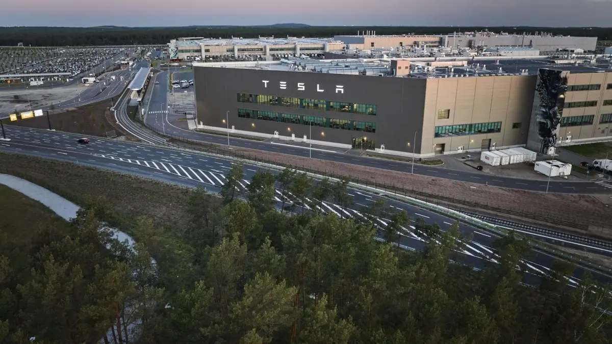 Tesla-Fabrik Grünheide: Blick am frühen Morgen auf ein kleines Waldstück im Vordergrund und dem Tesla-Werk im Hintergrund. (zu dpa: «Neuer Wasservertrag für Tesla geplant - Verband entscheidet»)