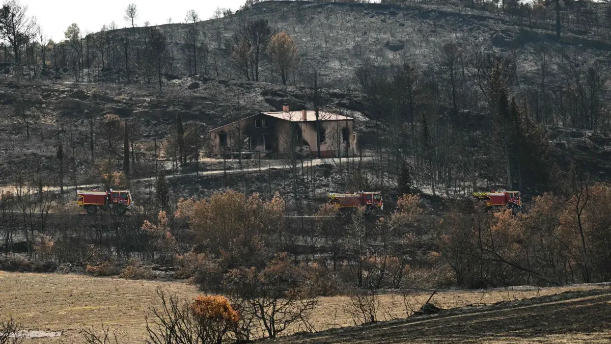 Brand in Südfrankreich: 10.08.2025, Frankreich, Jonquières: Feuerwehrfahrzeuge fahren in Jonquières in Südfrankreich an verbrannter Vegetation und einem ausgebrannten Haus vorbei. Ein großer Flächenbrand in Südfrankreich hält die Feuerwehr noch immer in Atem. Foto: Bertrand Guay/AFP/dpa +++ dpa-Bildfunk +++