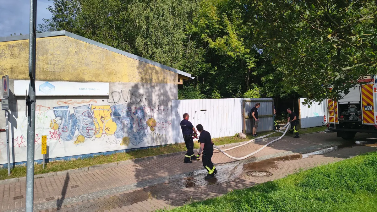 Die Berufsfeuerwehr Eberswalde kurz vor Beendigung ihres Einsatzes an der Bollwerkstraße. Hinter dem weißen Metallzaun erstreckt sich ein großes Gelände mit verfallenen Gebäuden.