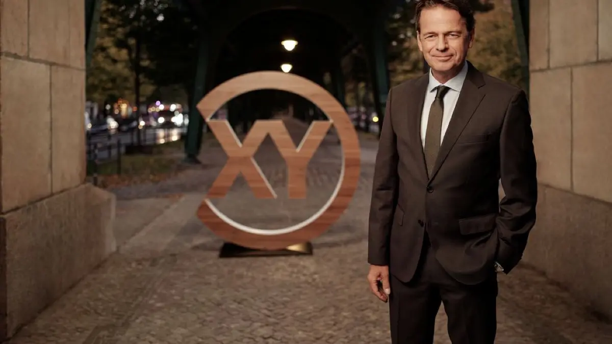 "Aktenzeichen XY… Ungelöst": Rudi Cerne steht vor dem "XY"-Logo und lächelt in die Kamera.