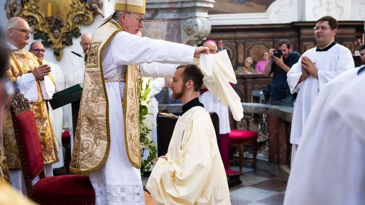 Zisterziensermönch im Kloster Neuzelle: 22.08.2025, Brandenburg, Neuzelle: Abt Maximilian Heim (l) bekleidet bei der feierlichen Profess Frater Christoph Benedikt Seemann OCist (M) mit einer geweihten Mönchskutte. Erstmals seit fast 209 Jahren legt wieder ein Zisterziensermönch im Kloster Neuzelle die ewigen Gelübde ab. Foto: Christophe Gateau/dpa +++ dpa-Bildfunk +++