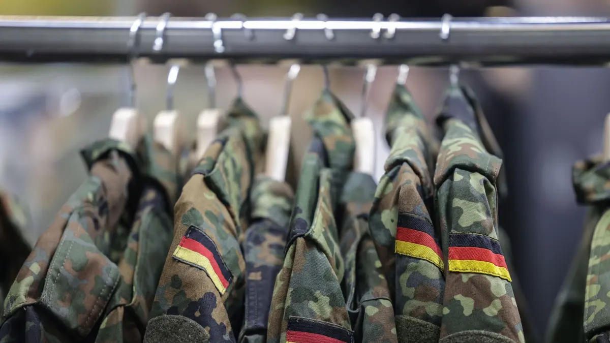 ARCHIV - 21.08.2025, Nordrhein-Westfalen, Köln: Feldjacken hängen am Stand der Bundeswehr bei der Computerspiele-Messe Gamescom (zu dpa: «CDU will Wehrpflicht-Automatismus im neuen Wehrdienst-Gesetz») Foto: Oliver Berg/dpa +++ dpa-Bildfunk +++