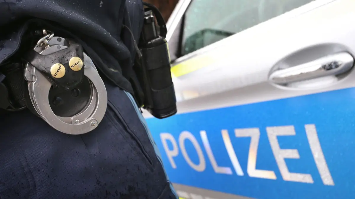 ARCHIV - 15.03.2019, Bayern, Kempten: ILLUSTRATION - Ein Polizist mit Handschellen und einer Pistole am Gürtel steht vor einem Streifenwagen. (zu dpa: «Raubüberfälle auf Tankstellen - zwei Männer festgenommen») Foto: Karl-Josef Hildenbrand/dpa +++ dpa-Bildfunk +++