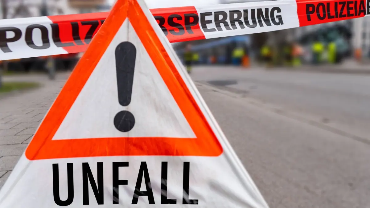 Bavaria, Germany - August 18, 2025: PHOTO MONTAGE, A warning sign with the word Accident next to police barrier tape. Symbolizes the diversion of a closed road due to ongoing police operations following a traffic accident. *** FOTOMONTAGE, Ein Warnschild mit der Aufschrift Unfall neben Absperrband der Polizei. Symbol für Umleitung einer gesperrten StraÃe durch laufenden Einsatz der Polizei durch Verkehrsunfall.