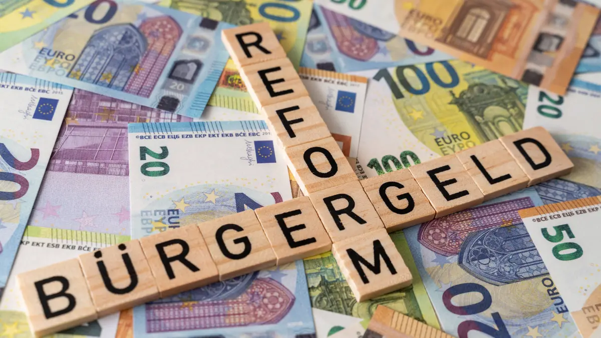 Die Bürgergeld-Reform steht an. Holzbuchstaben, die auf Geldscheinen gelegt sind und die Worte Bürgergeld und Reform bilden.
