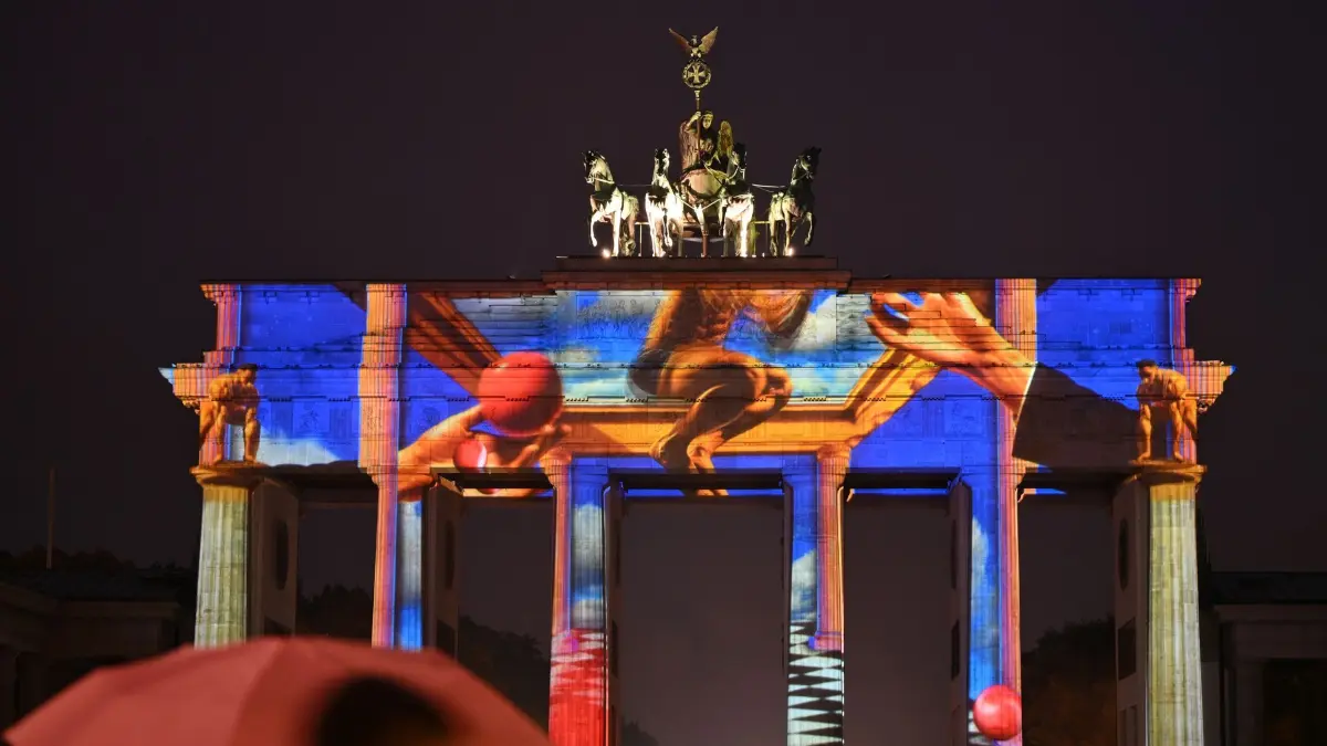 21. Festival of Lights startet in Berlin: ARCHIV - 08.10.2025, Berlin: Ein Mann mit Regenschirm steht vor dem erleuchteten Brandenburger Tor. Das 21. Festival of Lights steht unter dem Motto: «Let's shine together». Foto: Lilli Frter/dpa - ACHTUNG: Nur zur redaktionellen Verwendung im Zusammenhang mit der aktuellen Berichterstattung über das Festival of Lights und nur mit vollständiger Nennung des vorstehenden Credits +++ dpa-Bildfunk +++