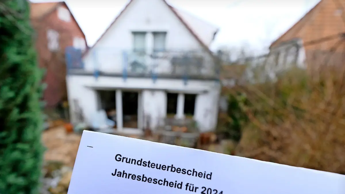 ARCHIV - 22.01.2024, Baden-Württemberg, Stuttgart: Ein Grundsteuerbescheid für 2024 wird vor einem Privatgrundstück hochgehalten. (zu dpa: «Was die neue Grundsteuer für Hausbesitzer und Mieter heißt») Foto: Bernd Weißbrod/dpa +++ dpa-Bildfunk +++