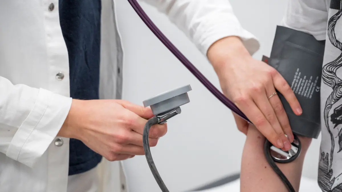 Medizinstipendiatin beginnt Facharztausbildung: PRODUKTION - 20.03.2024, Bayern, Schwarzenbach An Der Saale: Fanny Bartsch (l) kontrolliert den Blutdruck und den Puls eines Patienten (gestellte Szene). Die Medizinstipendiatin Fanny Bartsch hat ihr Medizinstudium erfolgreich abgeschlossen und beginnt ihre Facharztausbildung für Allgemeinmedizin in einer Praxis. (zu dpa: «In Budapest studieren, in der Westpfalz bleiben») Foto: Daniel Vogl/dpa +++ dpa-Bildfunk +++