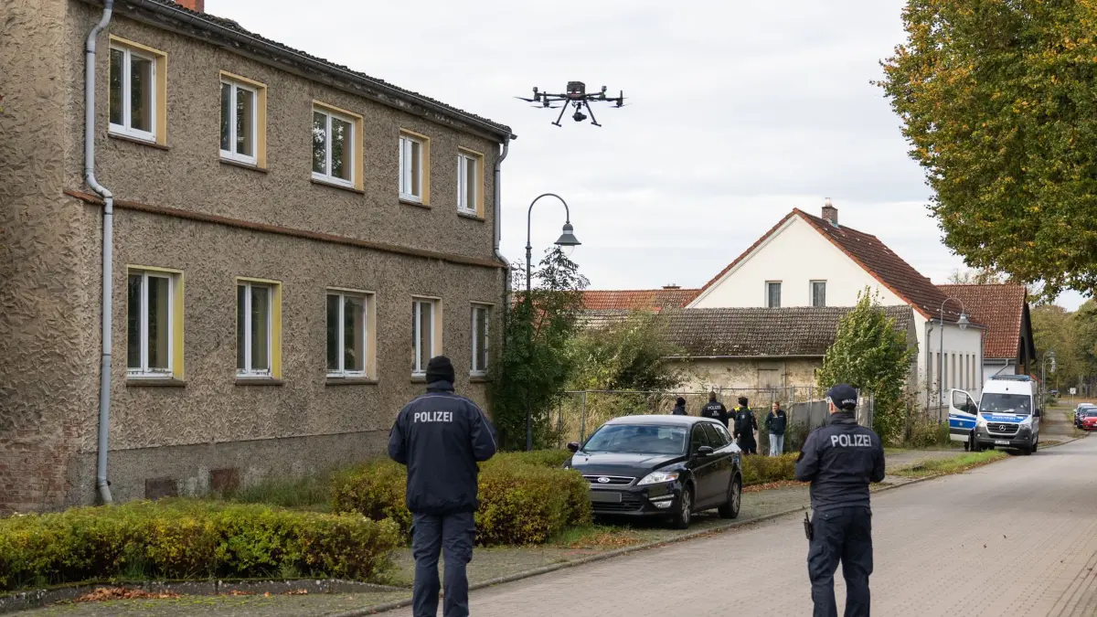 Polizei ermittelt im Fall Rebecca wegen eines Tötungsdelikts: 21.10.2025, Brandenburg, Tauche: Polizisten stehen vor einem Grundstück in Tauche (Landkreis Oder-Spree) und starten eine Drohne. Im Fall der seit mehr als sechs Jahren vermissten Rebecca aus Berlin-Neukölln sucht die Polizei auf einem Grundstück in Brandenburg nach Beweismitteln wegen des Verdachts eines Tötungsdelikts. Foto: Christophe Gateau/dpa - ACHTUNG: Das Kennzeichen wurde aus rechtlichen Gründen gepixelt. +++ dpa-Bildfunk +++