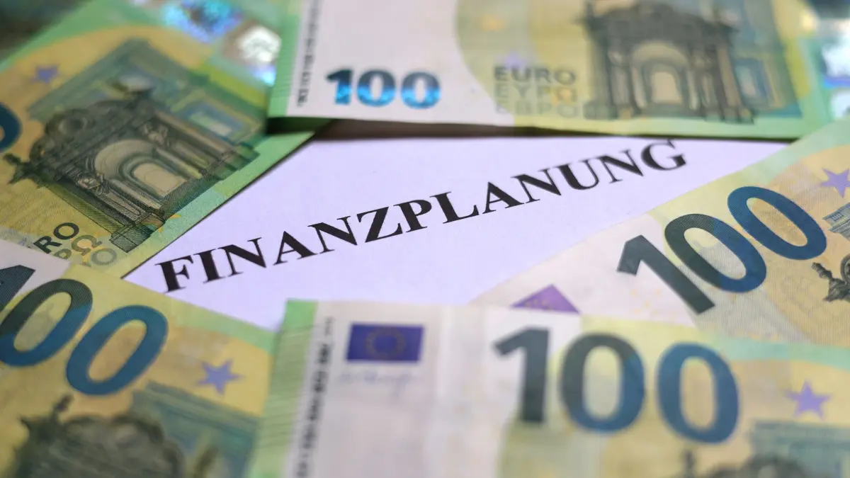 Symbolbild Geld: ILLUSTRATION - 03.06.2025, Bayern, Augsburg: 100-Euro-Banknoten liegen um das Wort «Finanzplanung». (zu dpa: «Drei hessische Städte erhalten den «Spar-Euro»») Foto: Karl-Josef Hildenbrand/dpa +++ dpa-Bildfunk +++