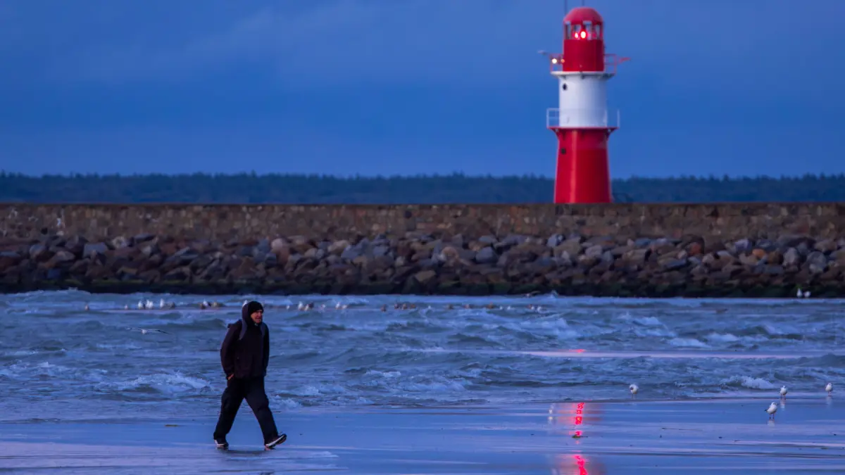 Ein Mann geht bei kräftigem Wind am Strand von Warnemünde nach dem Sonnenuntergang an der Ostsee entlang. An der Ostseeküste in Mecklenburg-Vorpommern wird laut Meteorologen stürmisches Wetter mit teilweise kräftigem Regen erwartet. +++ dpa-Bildfunk +++