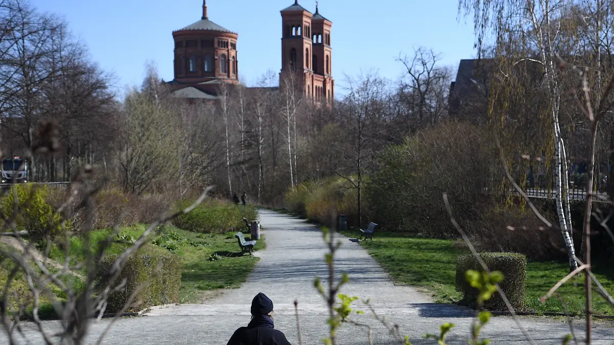 Eine junge Frau sitzt alleine auf einer Bank vor der St.-Thomas-Kirche in Kreuzberg.