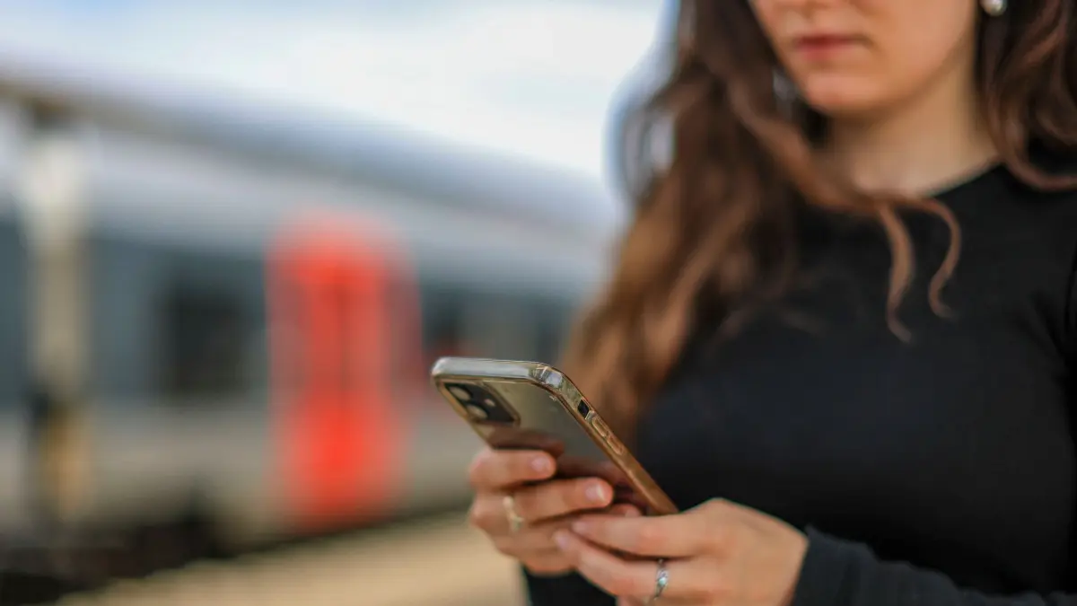 Eine junge Frau steht mit ihrem Mobiltelefon auf einem Bahnsteig