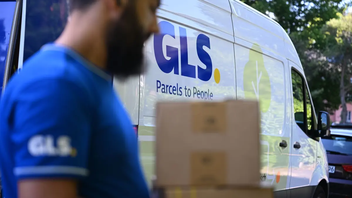 Paketbote von GLS: PRODUKTION - 04.07.2025, Nordrhein-Westfalen, Düsseldorf: Ein Paketbote des Paketdienstleisters GLS geht mit Paketen in der Hand an seinem Fahrzeug vorbei (gestellte Szene). GLS gehört hinter Marktführer DHL und den Konkurrenten Hermes, DPD und UPS zu den größeren Paketfirmen, die in Deutschland tätig sind. (zu dpa: «Verbraucher bestellen nur etwas mehr Pakete») Foto: Wolf von Dewitz/dpa +++ dpa-Bildfunk +++