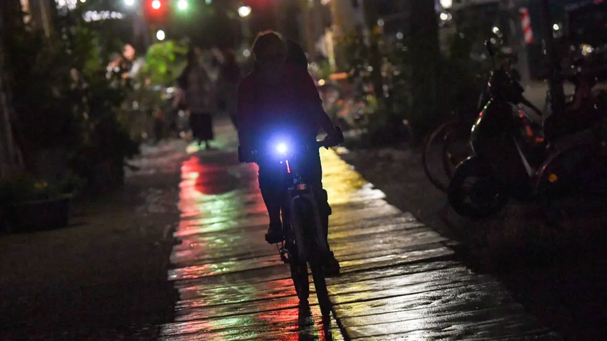 Radfahrer in der Nacht: ARCHIV - 09.08.2018, Berlin: Ein Fahrradfahrer fährt mit Licht in Kreuzberg am Abend in der Lübbener Straße auf einem nassen Gehweg, auf dem sich Lichter spiegeln. (zu dpa: «Polizei kontrolliert Verkehrsbeleuchtung - fast 750 Verstöße») Foto: Jens Kalaene/dpa-Zentralbild/dpa +++ dpa-Bildfunk +++