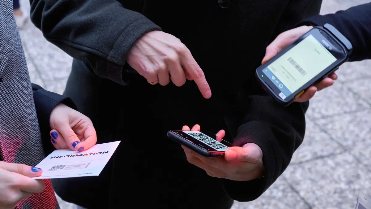 Ein Mann zeigt auf einen QR-Code den eine Frau Scannt: ARCHIV - Digitale Tickets lassen sich am einfachsten in Wallet-Apps speichern: So sind sie auch ohne Internet schnell griffbereit. (zu dpa: «Stress am Schalter: Damit es mit dem digitalen Ticket klappt») Foto: Annette Riedl/dpa/dpa-tmn - Honorarfrei nur für Bezieher des dpa-Themendienstes +++ dpa-Themendienst +++