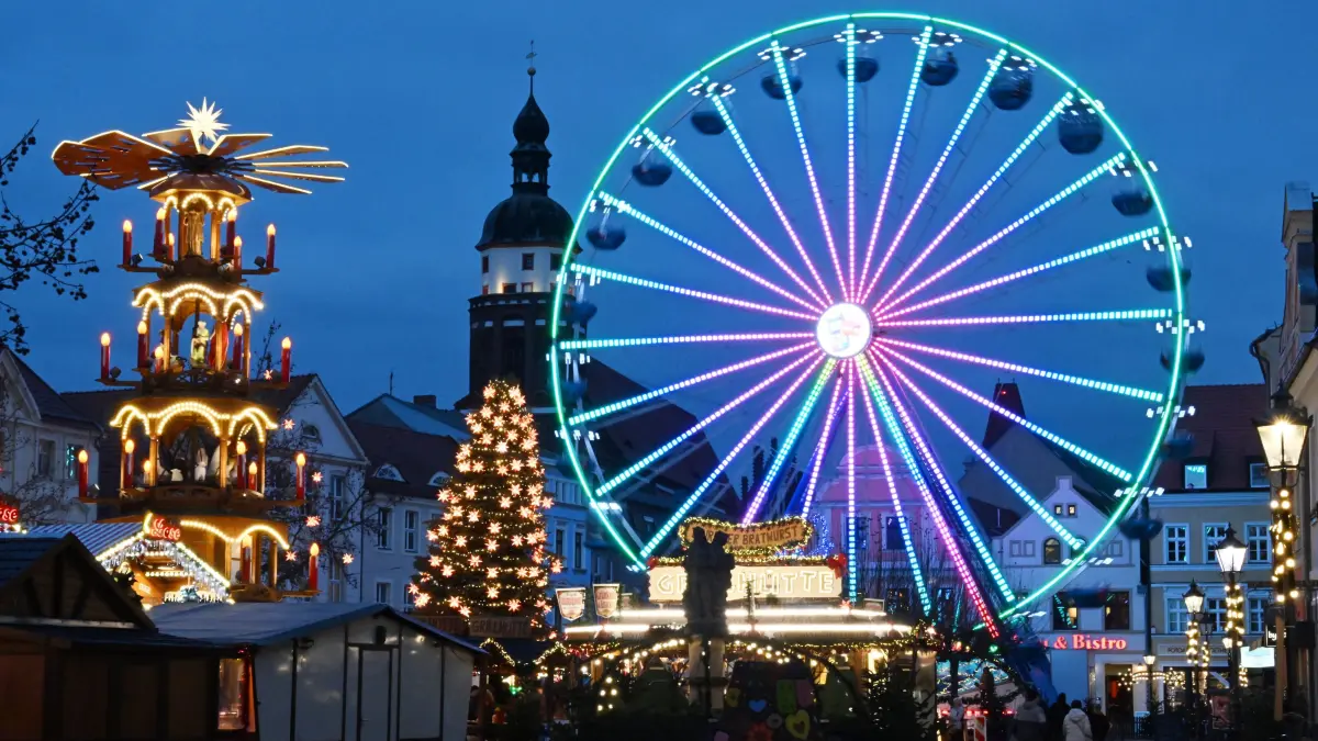 Weihnachtsmarkt 2025 Abend: Blick auf den abendlichen Cottbuser Weihnachtsmarkt der 1000 Sterne. Täglich lädt er von 11 bis 19 Uhr zum Bummeln und Verweilen ein. Er endet auf dem Altmarkt am 28. Dezember 2025. Tags zuvor, am 27.Dezember, gibt es auf dem Altmarkt den traditionellen Rückkehrertag. Die Marktteile in der Spremberger Strasse sowie am Platz am Stadtbrunnen enden bereits am 23. Dezember 2025. Die Gastronomie öffnet bis 21.00 Uhr. In diesem Jahr sind rund 90 Händler bzw. Teilnehmer vertreten. Dazu zählen auch 15 Glühweinstände.
Ein besonderes Highlight ist in diesem Jahr die Rückkehr einer echten Eisbahn. Das erste Mal seit vielen Jahren gibt es wieder eine echte Eisbahn mit richtigem Eis statt Kunststoff zum Schlittschuhlaufen. Die Bahn 29,5 mal 12 Meter große Bahn befindet sich am Postparkplatz in der Stadtpromenade zwischen Eventfläche und Flaniermeile. Am Rand der Eisbahn können sich die Besucher an Imbiss- und Getränkeständen stärken.