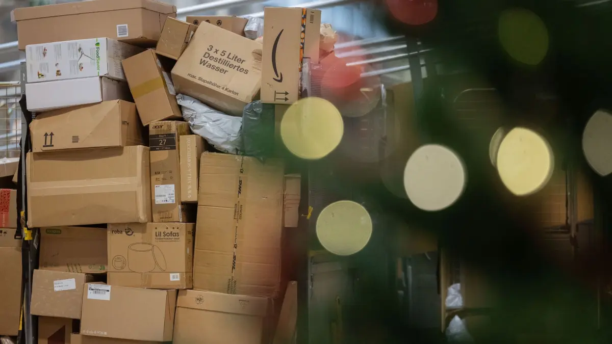 Paketbeförderung in der Vorweihnachtszeit: PRODUKTION - 04.12.2025, Nordrhein-Westfalen, Köln: Pakete sind in einer Zustellbasis von Deutsche Post DHL hinter einem Weihnachtsbaum zu sehen. Aktuell fallen durch den Black Friday (Black Week) und Weihnachten mehr Pakete an. Im diesjährigen Weihnachtsgeschäft rechnet die Deutsche Post DHL wieder mit Paketmassen. Foto: Rolf Vennenbernd/dpa +++ dpa-Bildfunk +++
